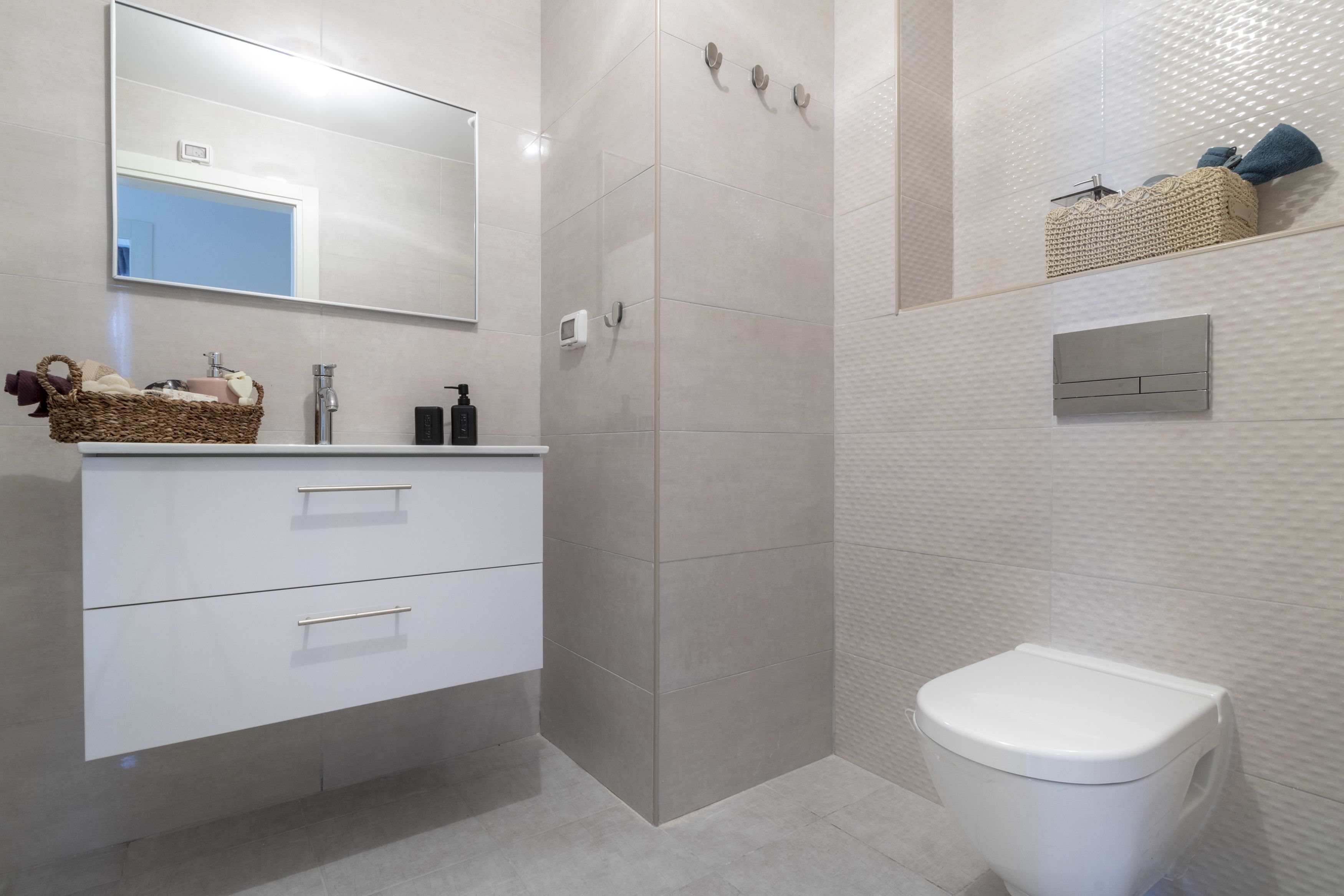 Une salle de bain moderne avec un meuble-lavabo blanc, un grand miroir, une cabine de douche et des toilettes.