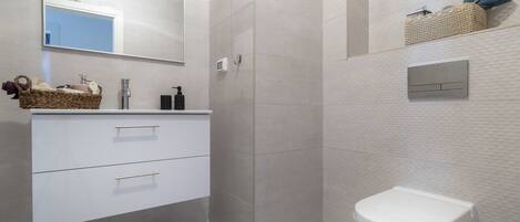 Une salle de bain moderne avec un meuble-lavabo blanc, un grand miroir, une cabine de douche et des toilettes.