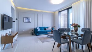 A modern living room with a blue sofa, a glass dining table, and a TV mounted on the wall. - JTower - Isrentals (Jerusalem)