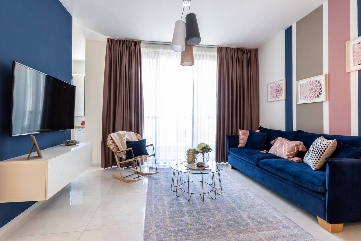 Uma sala de estar moderna com um sofá azul, uma televisão, uma poltrona de balanço e uma mesa de centro.