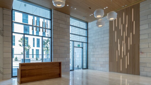 A spacious lobby with large windows, a wooden reception desk, and modern pendant lighting. - JTower - Isrentals (Jerusalem)