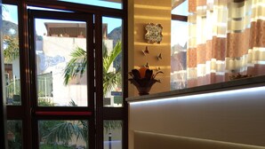 Zona de recepción con puerta de vidrio que da al exterior, mostrador de recepción y una planta en maceta.