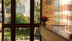 Zona de recepción de hotel con puerta de vidrio que da a un patio, mostrador de recepción y decoración en la pared.