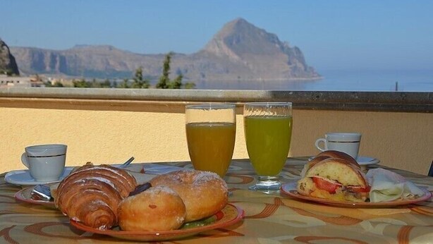 Una mesa con cruasanes, un sándwich y dos tazas de té, con vistas a un paisaje montañoso.