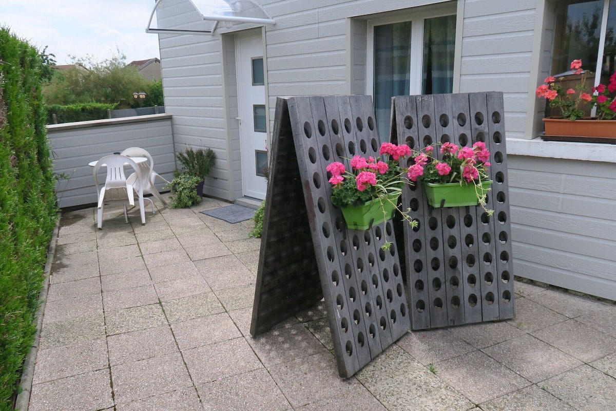 Un patio con una silla blanca, una mesa pequeña y dos macetas con flores rosadas.