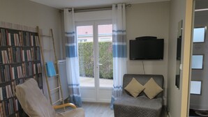 A room with a bookshelf, a chair, a sofa, a TV, and a window with curtains. - Les Collinades de Chalons (Fagnieres)
