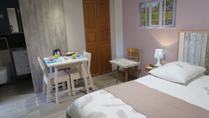A bedroom with a bed, a desk with breakfast items, a chair, a nightstand with a lamp, and a view of the outdoors through a window. - Les Collinades de Chalons (Fagnieres)