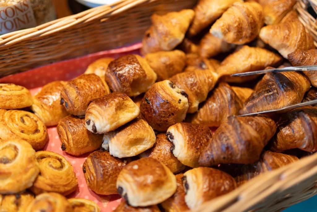 A variety of pastries, including croissants and chocolate-filled pastries, displayed in a basket.