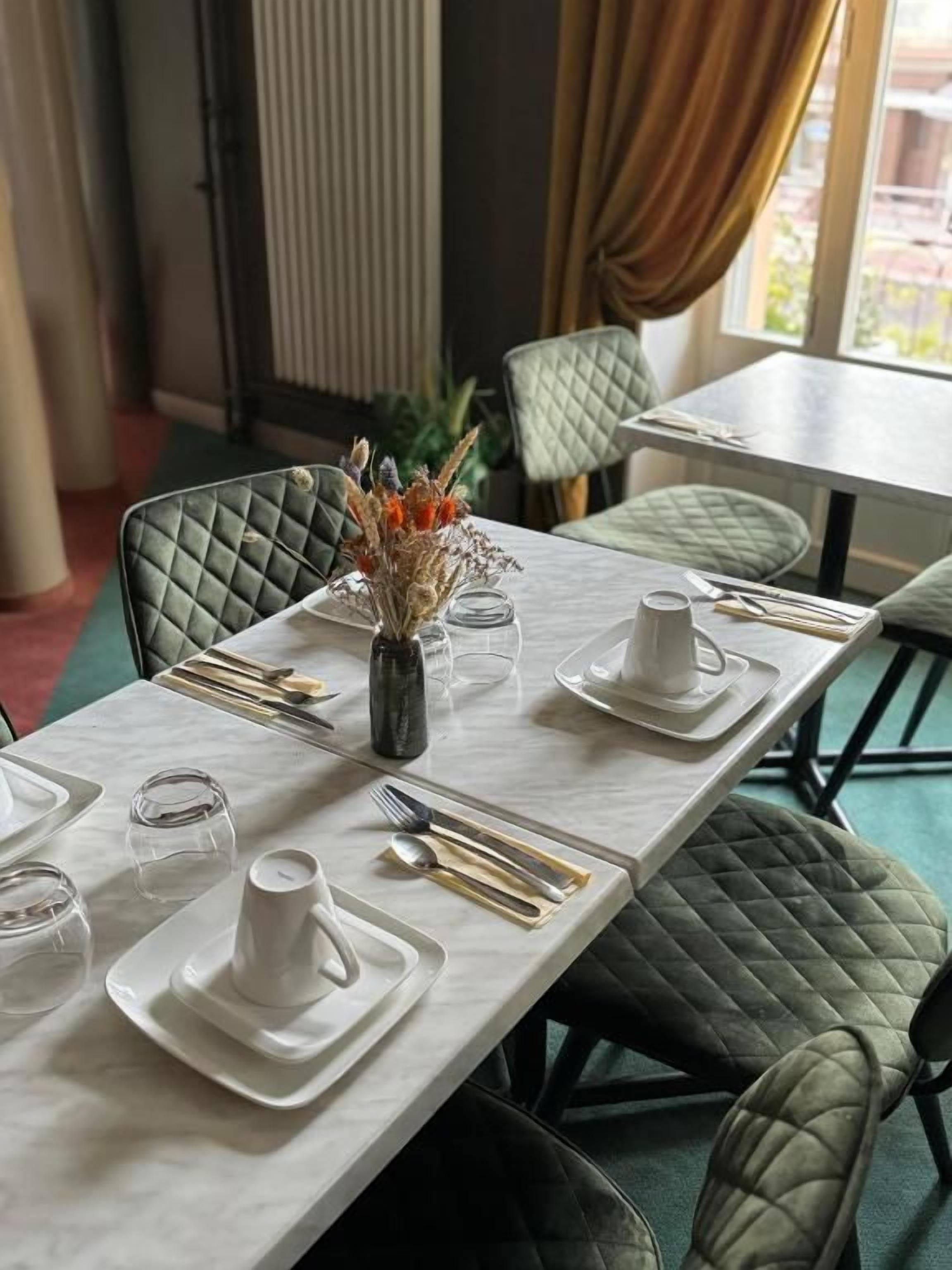 A dining table set with plates, cutlery, and a vase with dried flowers.