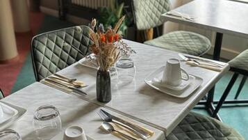 A dining table set with plates, cutlery, and a vase with dried flowers.