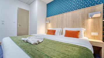 Een hotelkamer met een bed, een groene dekensprei en een blauw geometrisch patroon op de muur.