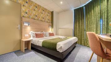Ein Hotelzimmer mit Bett, Nachttisch, Sessel und Schreibtisch mit Stuhl.