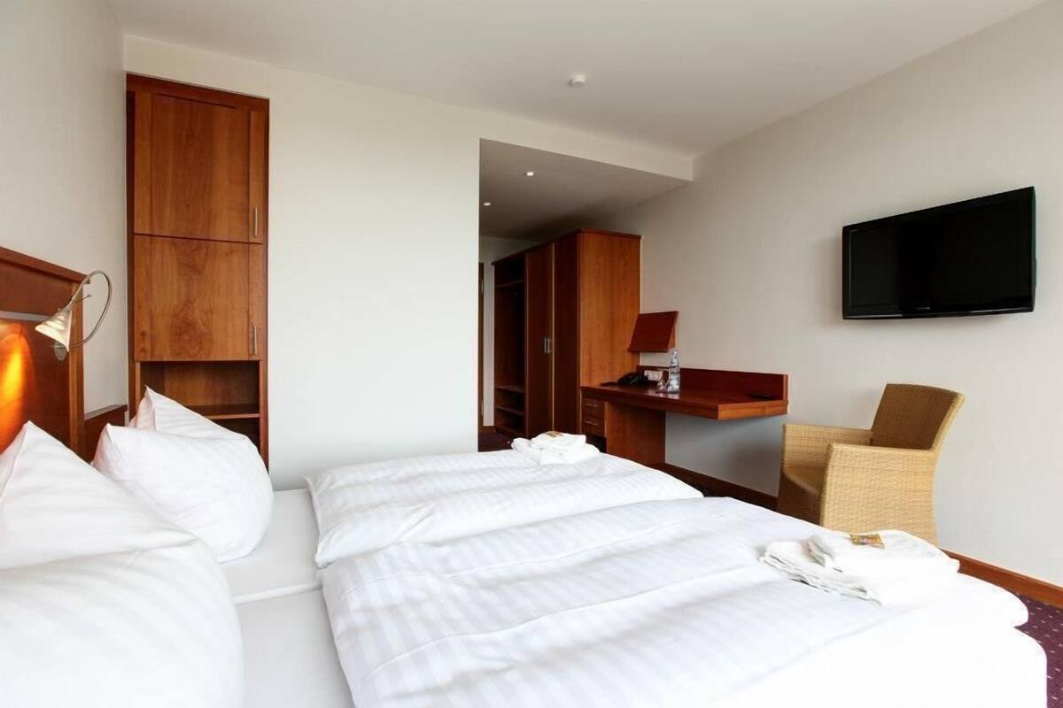 Habitación de hotel con una cama grande, un armario de madera, un escritorio con una silla y un televisor de pantalla plana montado en la pared.