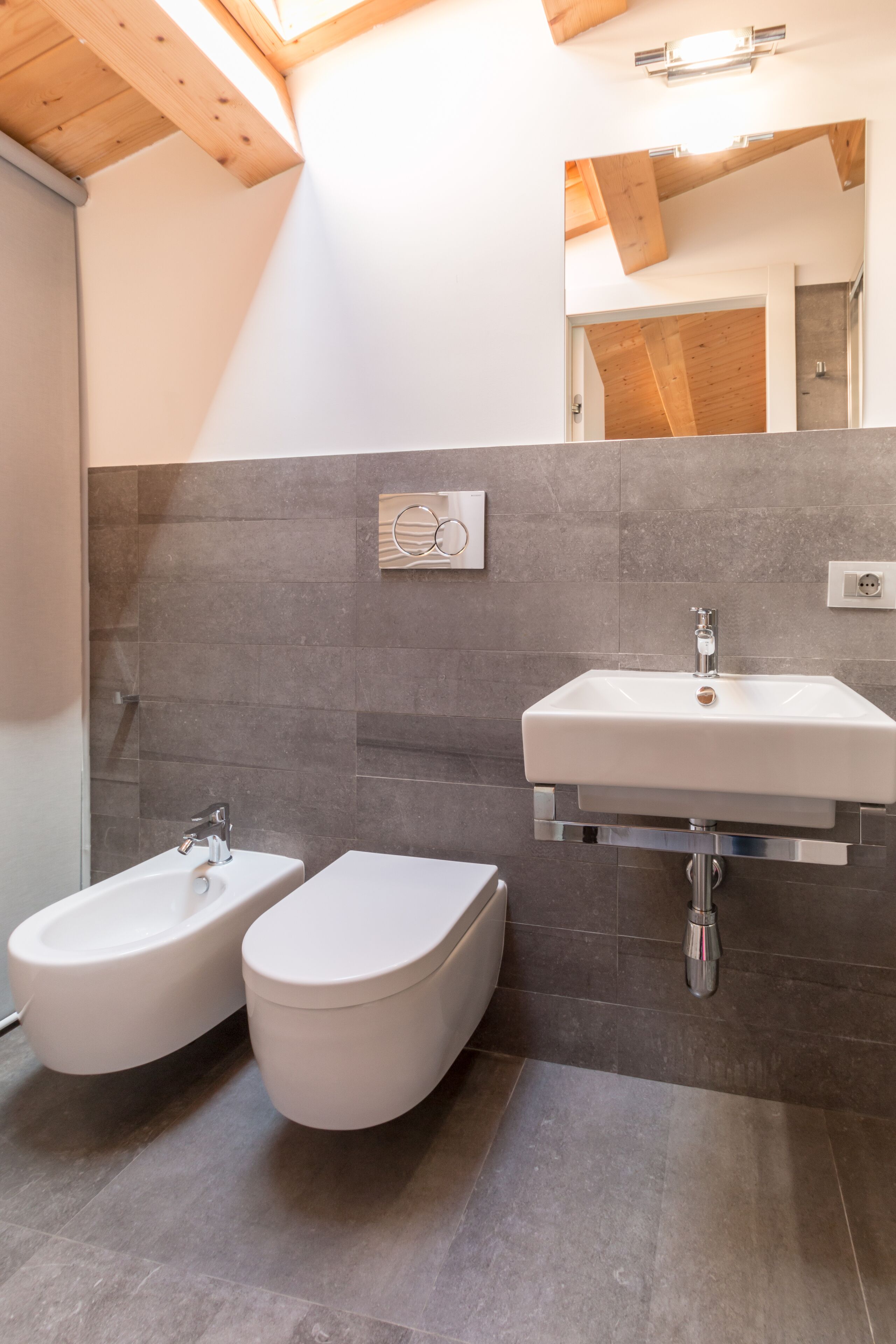A modern bathroom with a white sink, two toilets, and a shower.