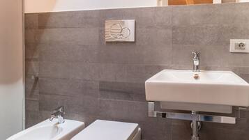 A modern bathroom with a white sink, two toilets, and a shower.