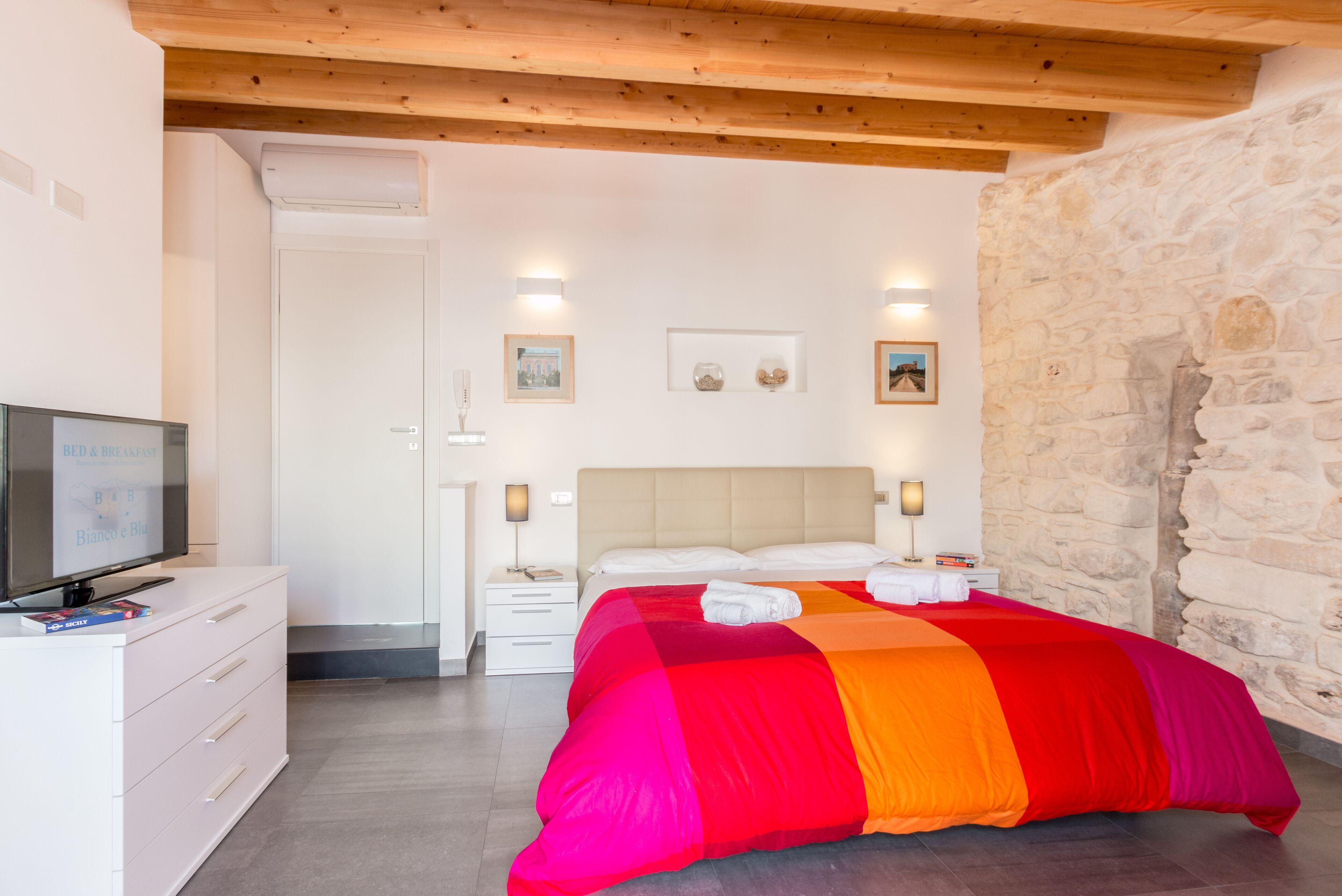 Un dormitorio con una cama, un televisor, un tocador y una pared de piedra.