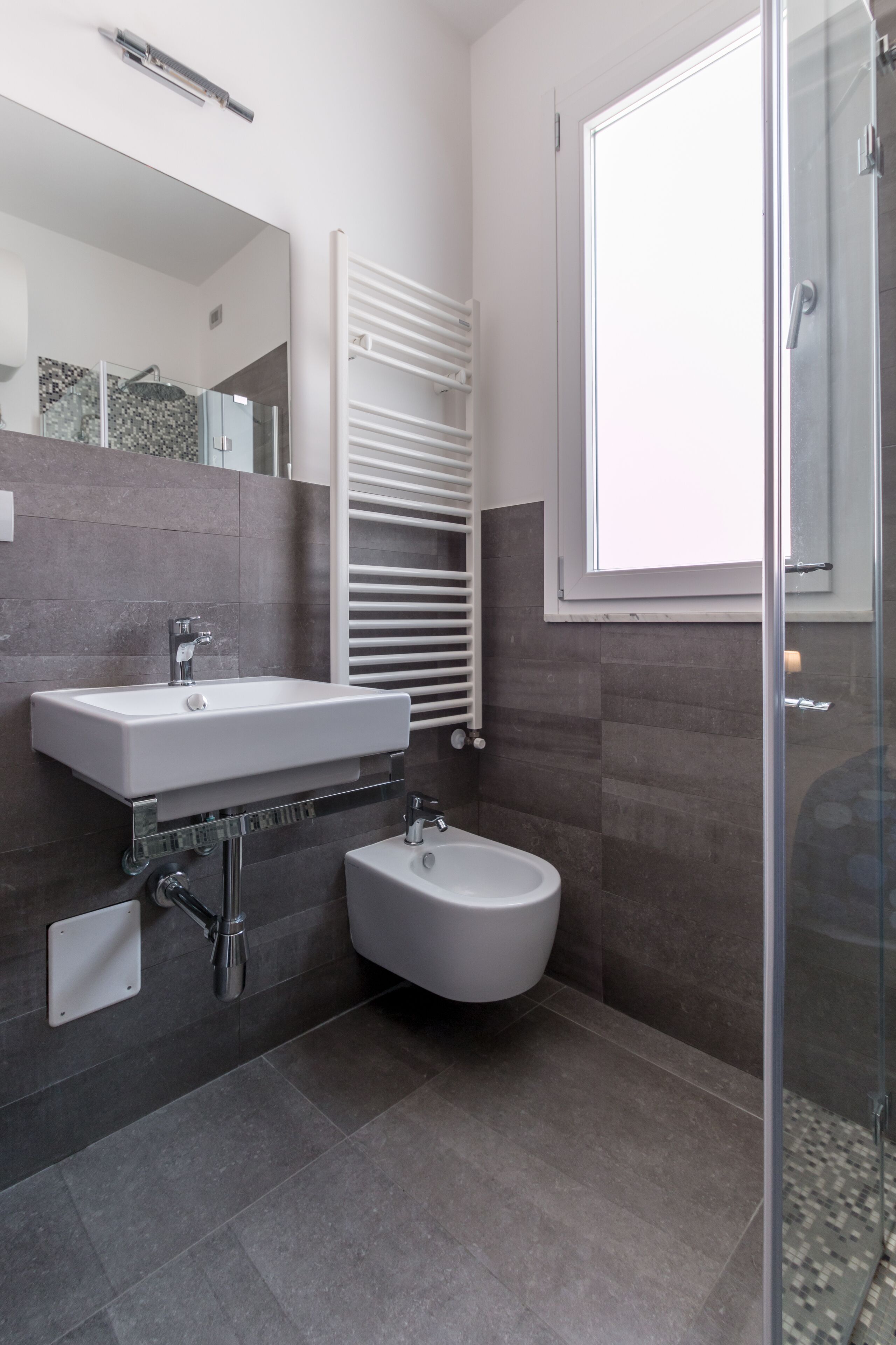 Et moderne badeværelse med hvid vask, bidet, brusekabine i glas og et håndklædetørrestativ.