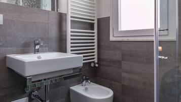 Et moderne badeværelse med hvid vask, bidet, brusekabine i glas og et håndklædetørrestativ.