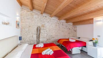 A bedroom with two beds, stone walls, wooden beams, and a small white cabinet with a plant.