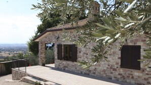 A stone building with a tiled roof, two windows with shutters, a small porch, and a view of the countryside. - B&B Lavanda e Rosmarino (Assisi)