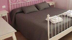 A bedroom with a pink wall, a white metal bed frame, a brown bedspread, two pillows, a bedside table with a lamp, and a painting of flowers on the wall. - B&B Lavanda e Rosmarino (Assisi)