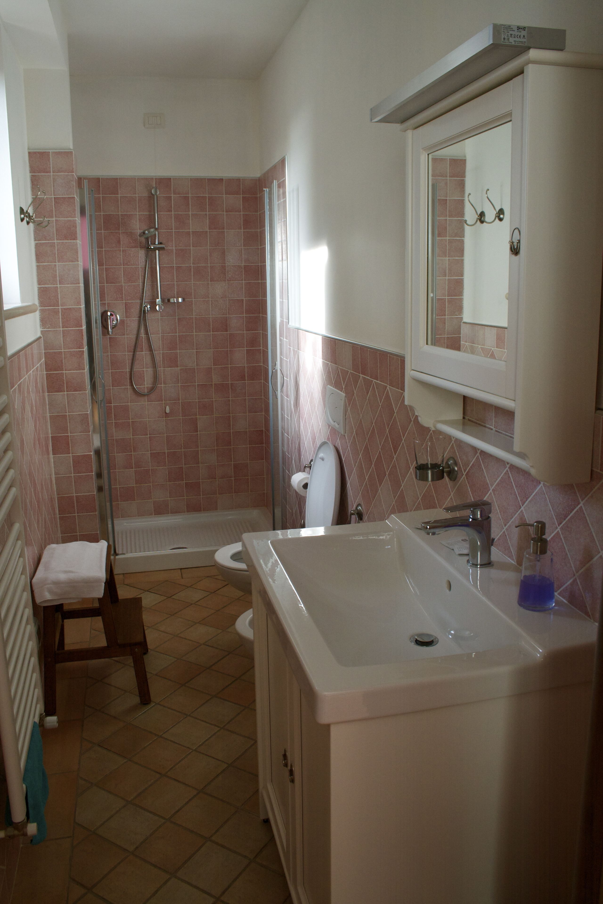 Un baño con ducha, inodoro, lavamanos y un taburete pequeño.