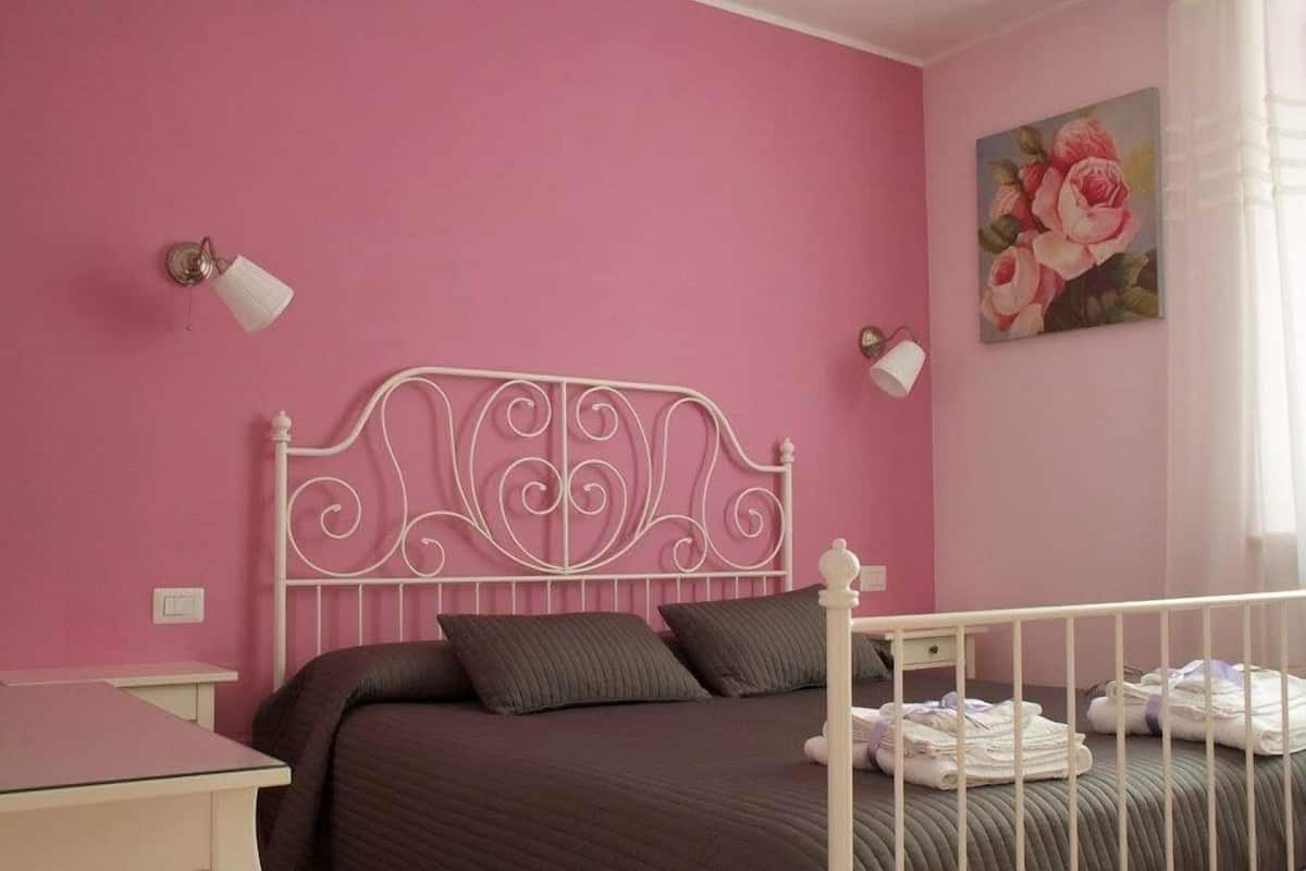 A pink-themed bedroom with a metal bed frame, dark bedding, and a bedside table with towels.