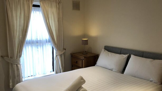 A neatly made bed with a rolled towel, a bedside lamp, and a nightstand. - North Circular Studios 2 (Dublin)