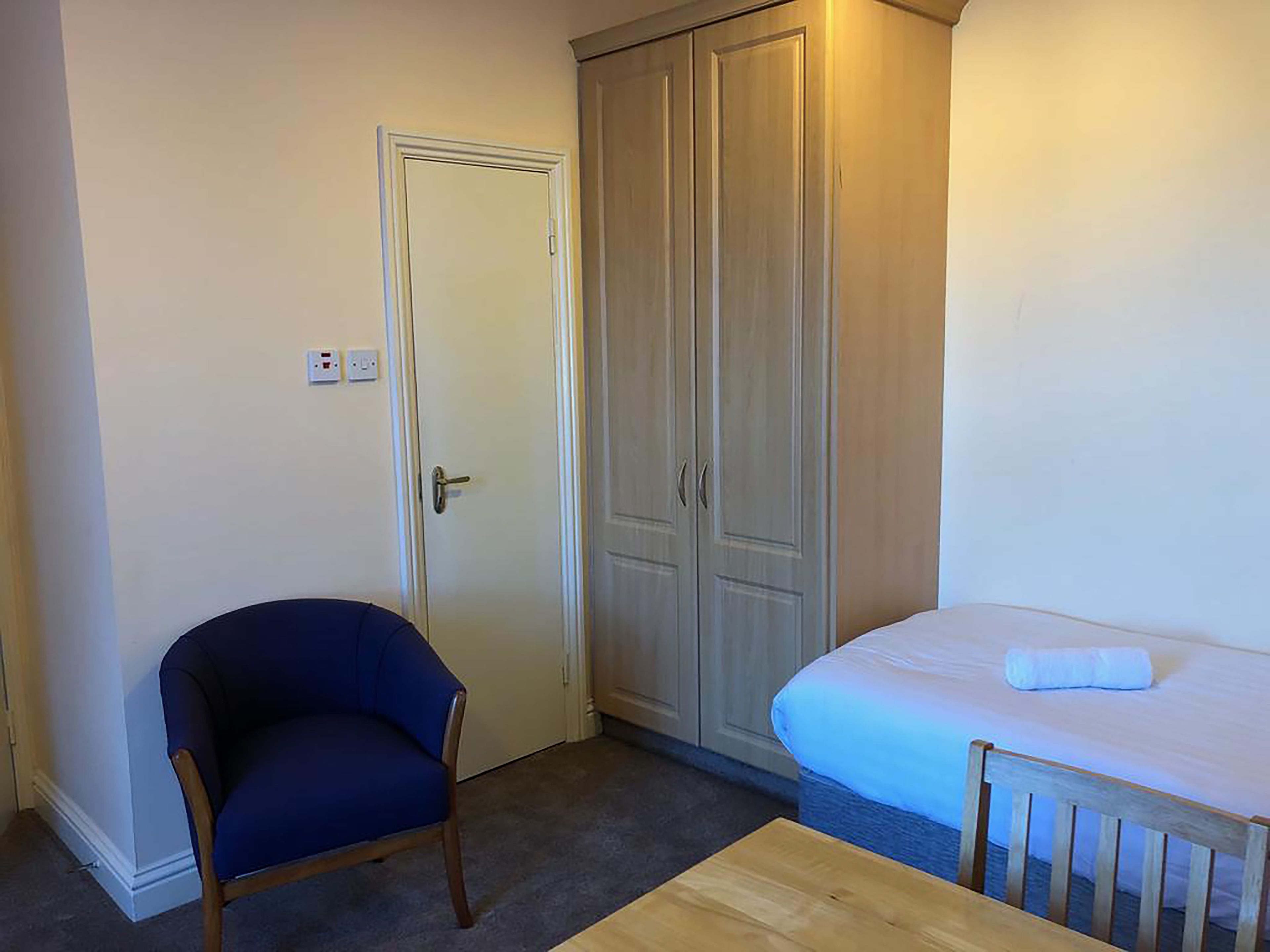 A small room with a single bed, a chair, and a wardrobe.