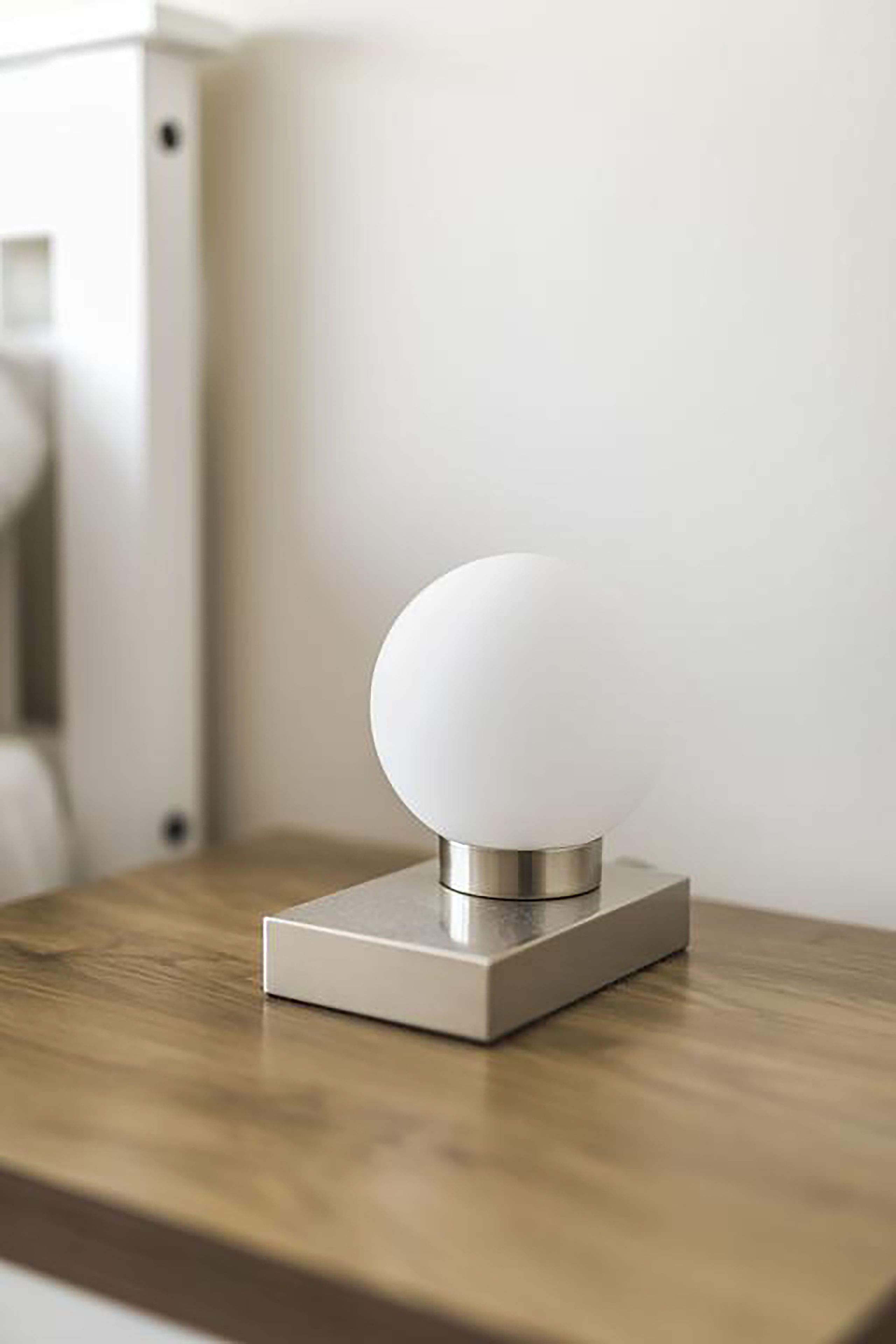 Une lampe de table moderne et minimaliste, dotée d’un abat-jour sphérique monté sur un socle rectangulaire, posée sur une surface en bois.