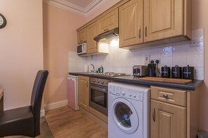 A compact kitchen with wooden cabinets, a microwave, a washing machine, and a coffee maker. - North Circular Studios 2 (Dublin)