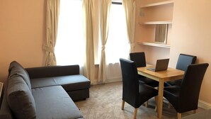 A modern living room with a sectional sofa, a dining table with chairs, and large windows with curtains. - North Circular Studios 2 (Dublin)
