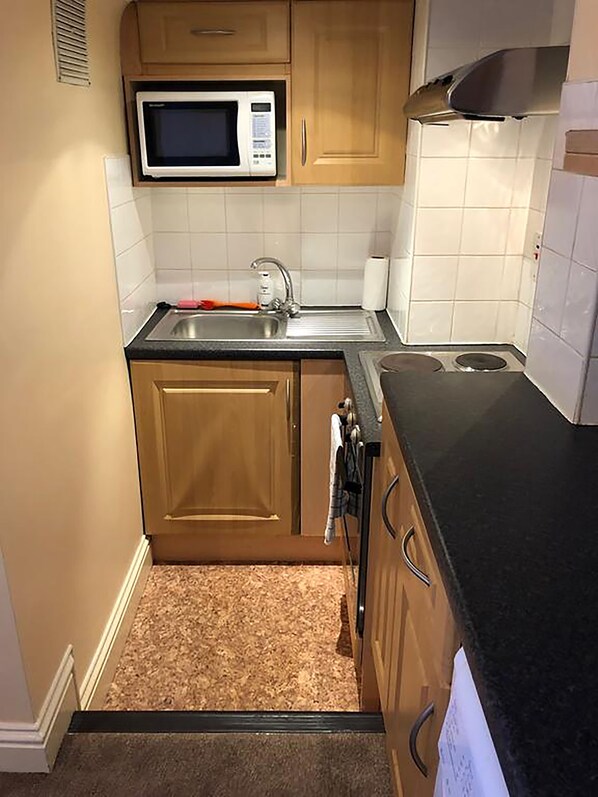 Cocina compacta con microondas, lavamanos y estufa.