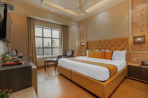 A hotel room with a large bed, a desk with a computer, a chair, a window with a city view, and a ceiling fan.