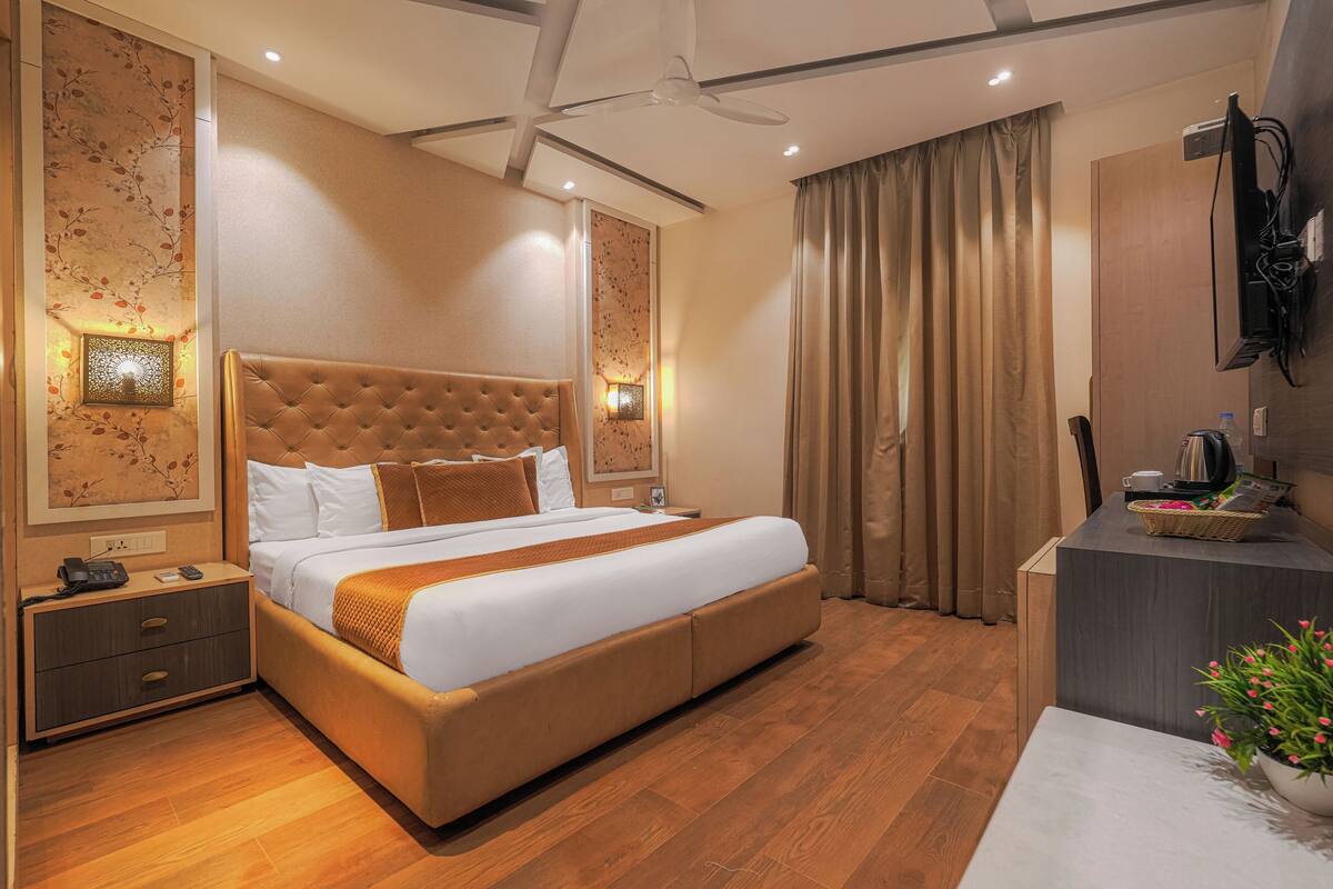 A hotel room with a large bed, a desk with a computer, a TV, and a ceiling fan.