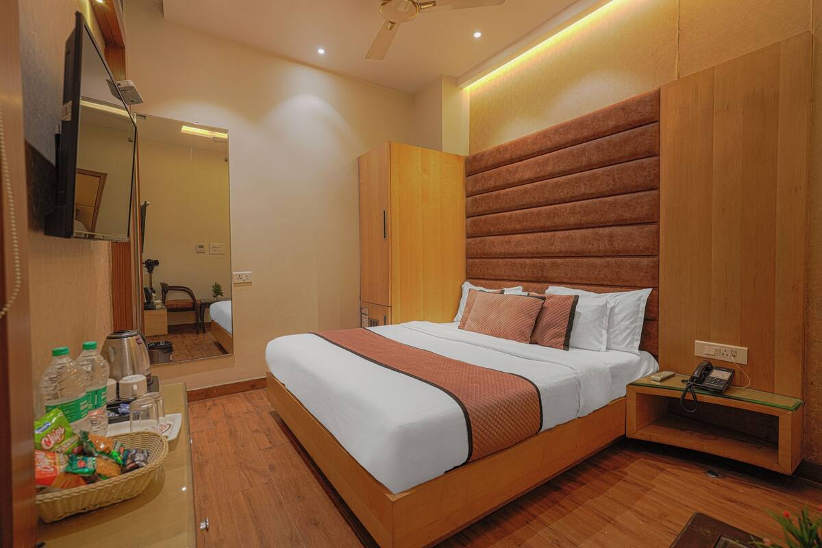 A modern hotel room with a large bed, wooden headboard, a bedside table with a phone, and a mirror on the wall.