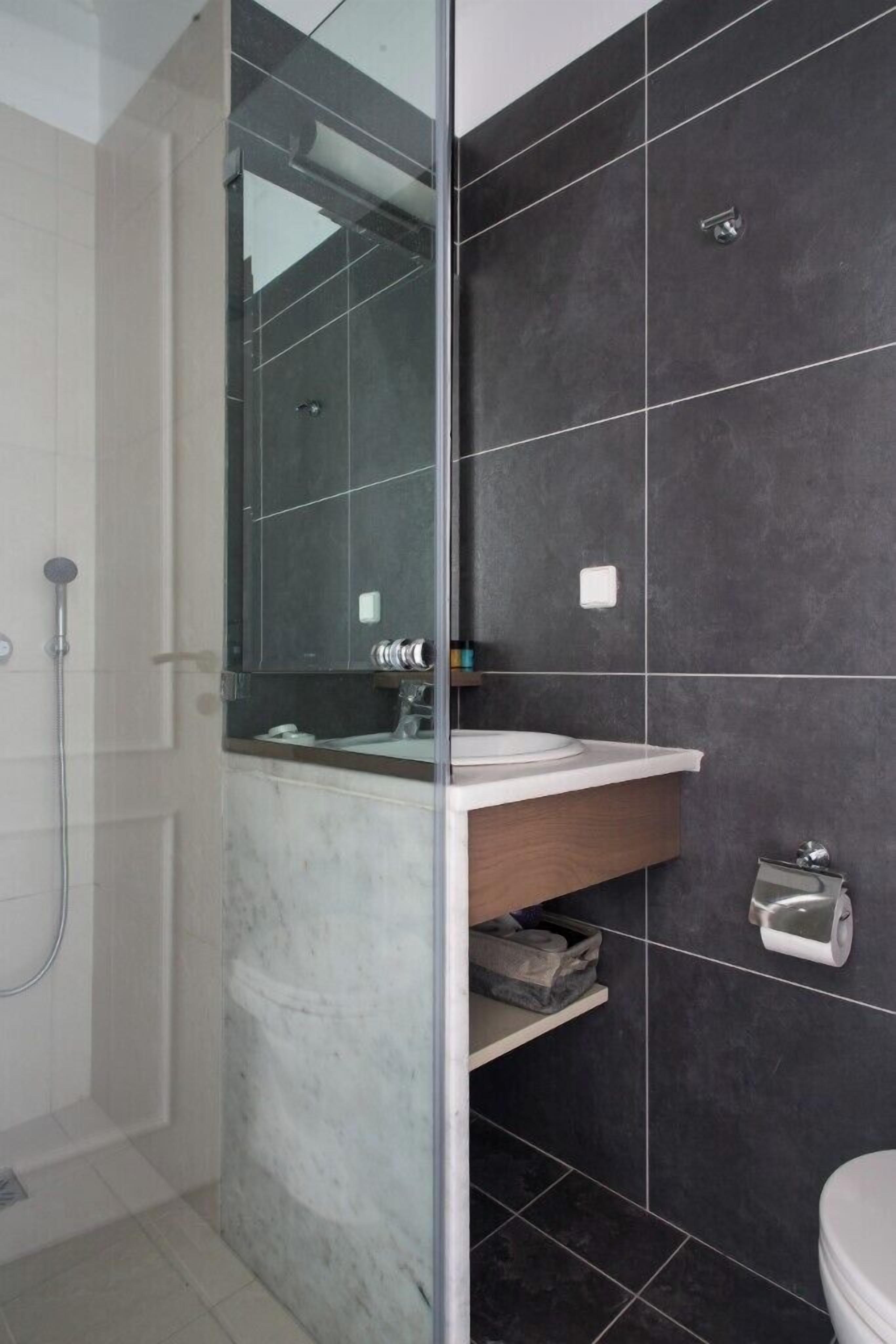 A modern bathroom with a glass shower enclosure, a marble sink, and dark tiled walls.