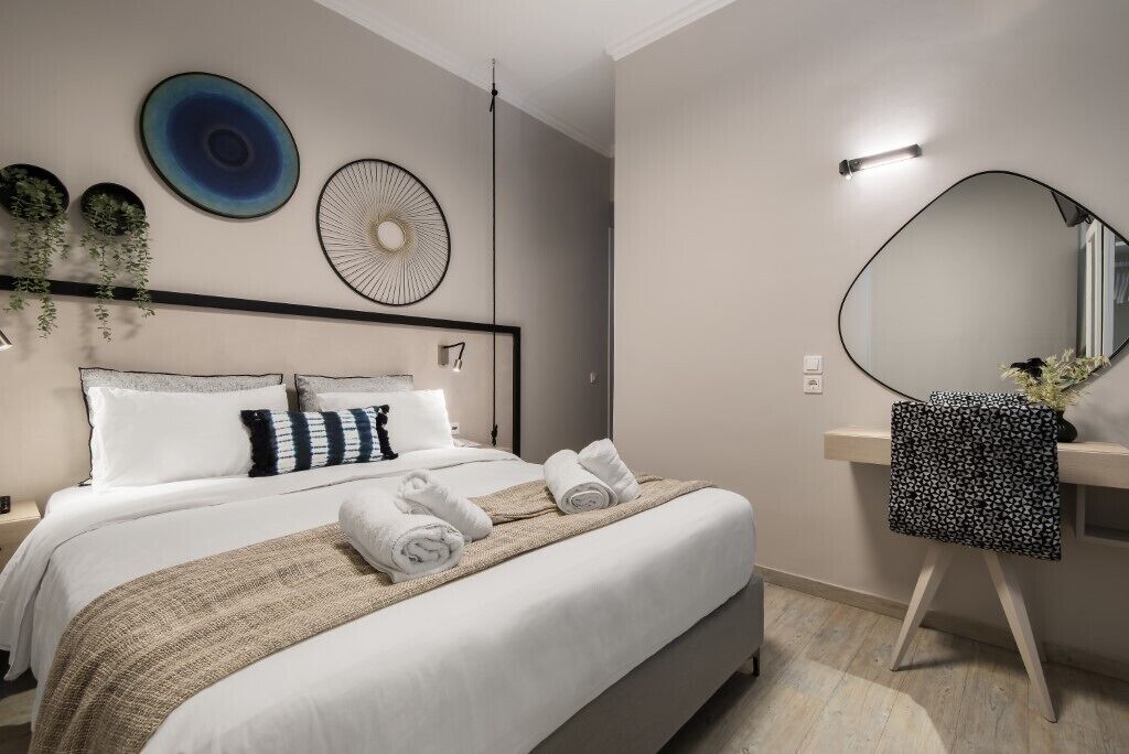 A modern hotel room with a large bed, a bedside table, a mirror, and decorative wall art.