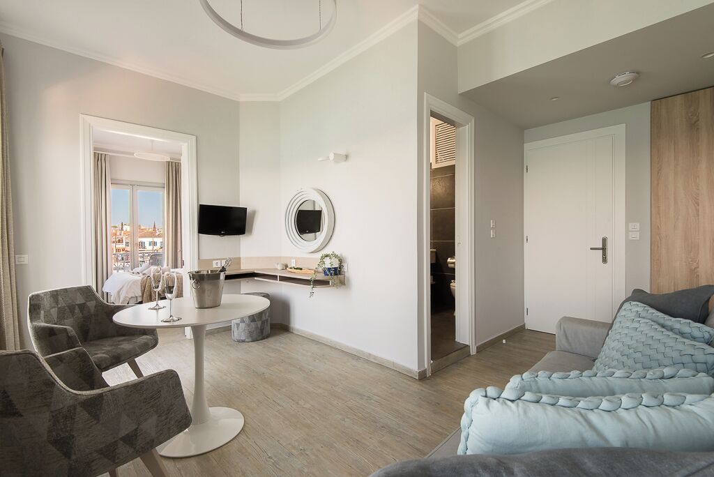 A modern hotel room with a seating area, a dining table, and a TV mounted on the wall.