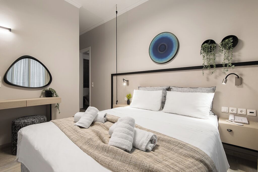 A modern hotel room with a neatly made bed, a bedside table with a lamp, and a wall-mounted plant.
