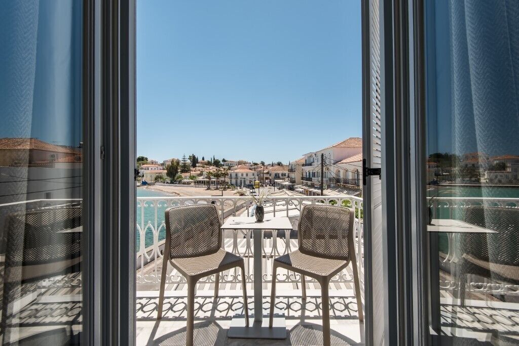 Ein Balkon mit zwei Stühlen und einem Tisch, mit Blick auf einen Pool und eine Wohngegend.