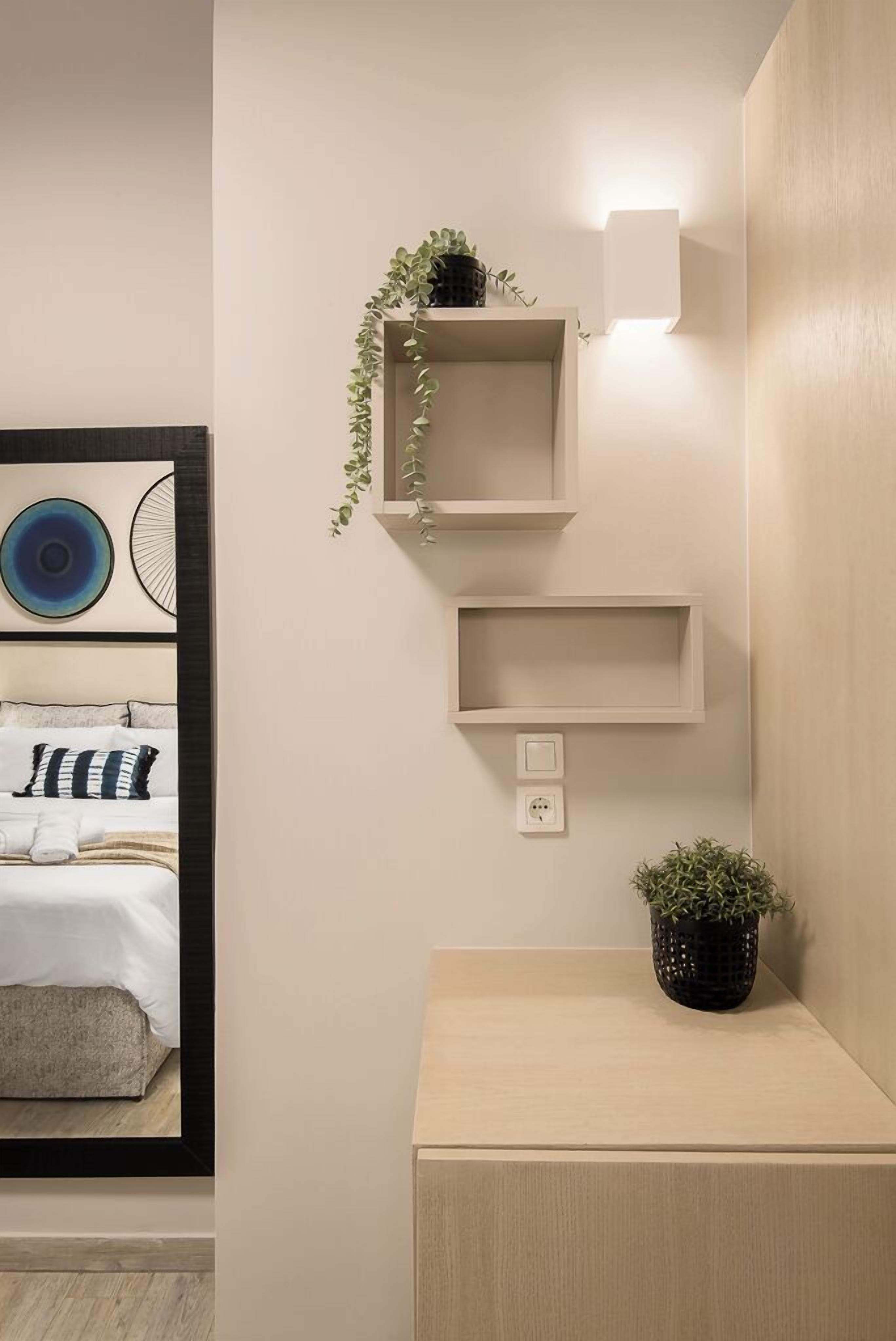 A modern room with a bed, a wall-mounted shelf with plants, and a small table.