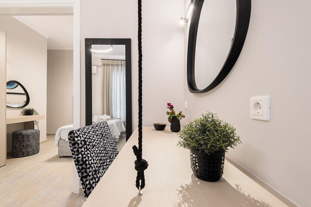 A modern hotel room with a large mirror, a black and white patterned sofa, a potted plant, and a small table.