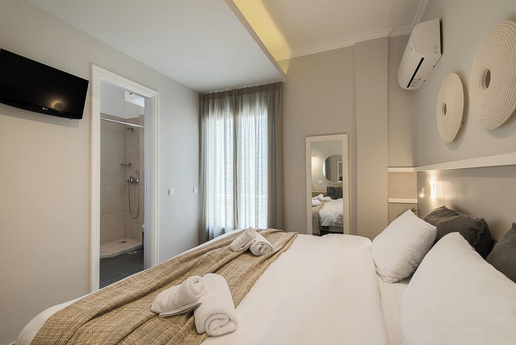 A hotel room with a bed, a TV, a shower, and a window with curtains.