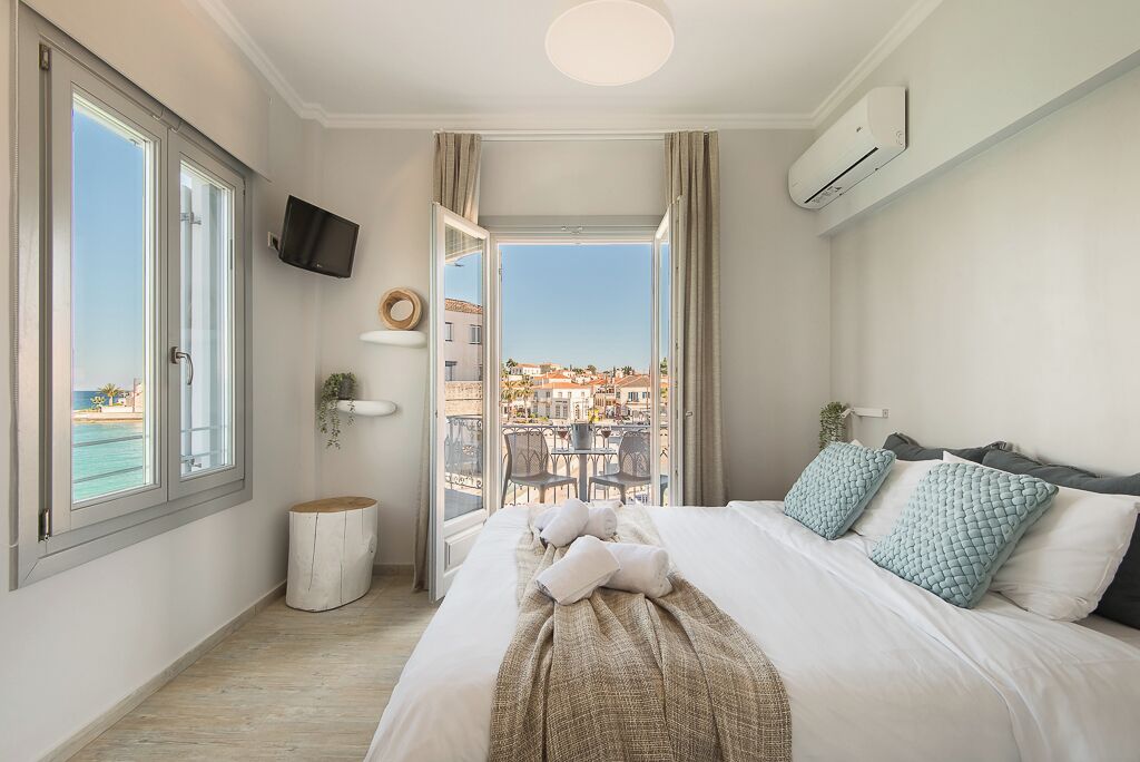 A hotel room with a bed, a TV, a view of the city, and an air conditioning unit.
