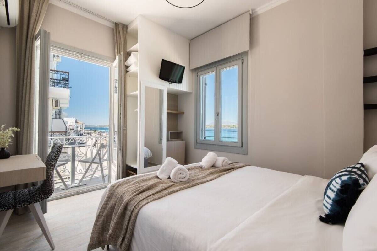 A hotel room with a bed, a desk, a chair, a TV, and a balcony with a view of the city.