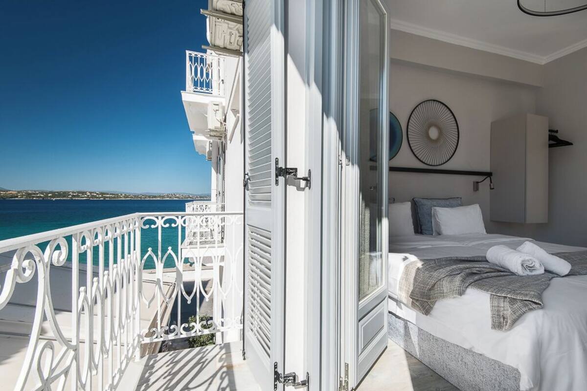 A bedroom with a bed, a view of the sea, and a balcony with white railings.