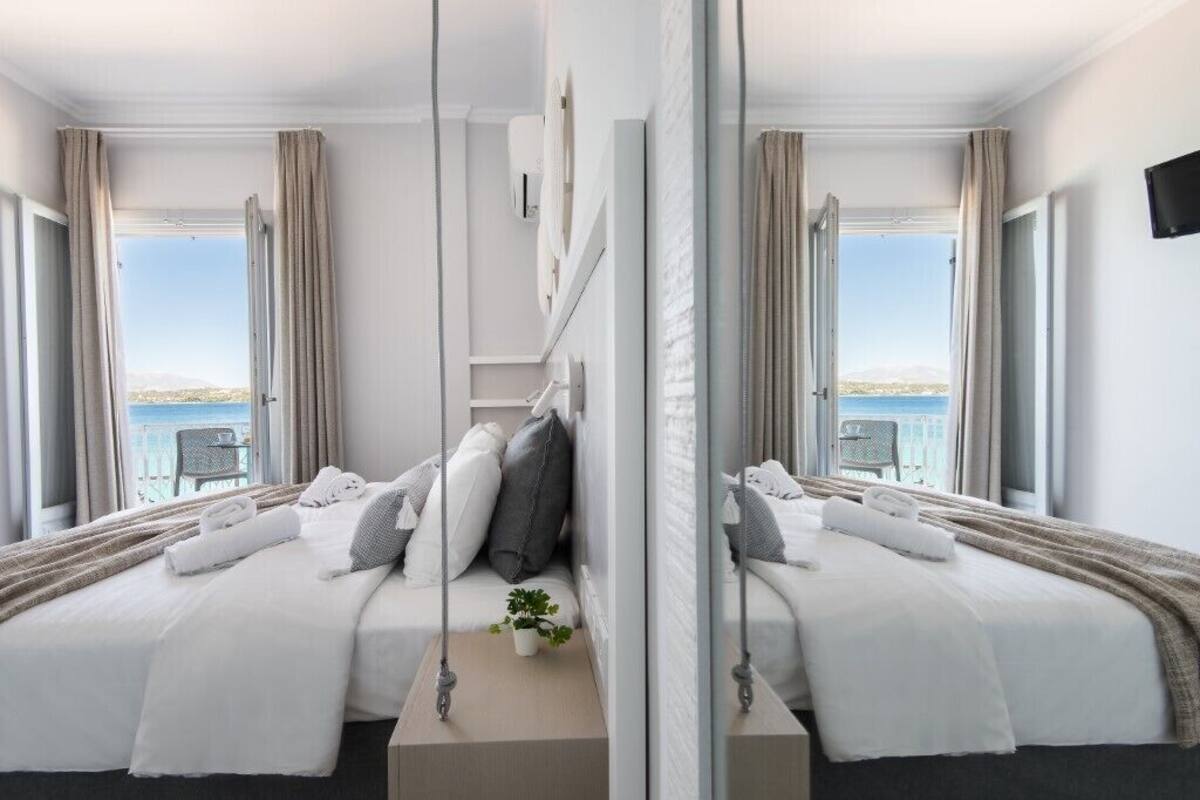 A hotel room with a bed, a small table with a plant, and a view of the sea.