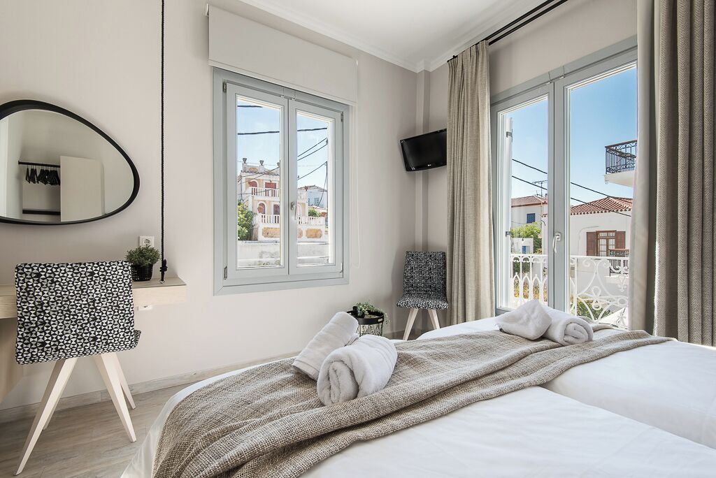A hotel room with a large bed, a desk, a chair, a TV, and a window with a view of buildings.