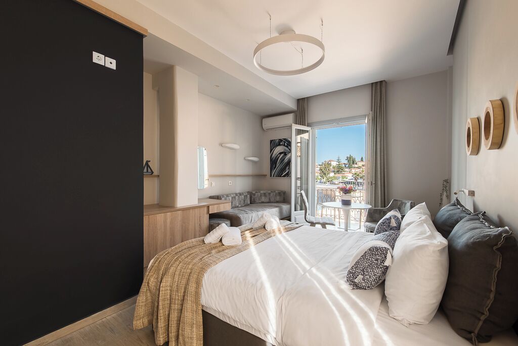 A modern hotel room with a large bed, a desk, and a balcony with a view.
